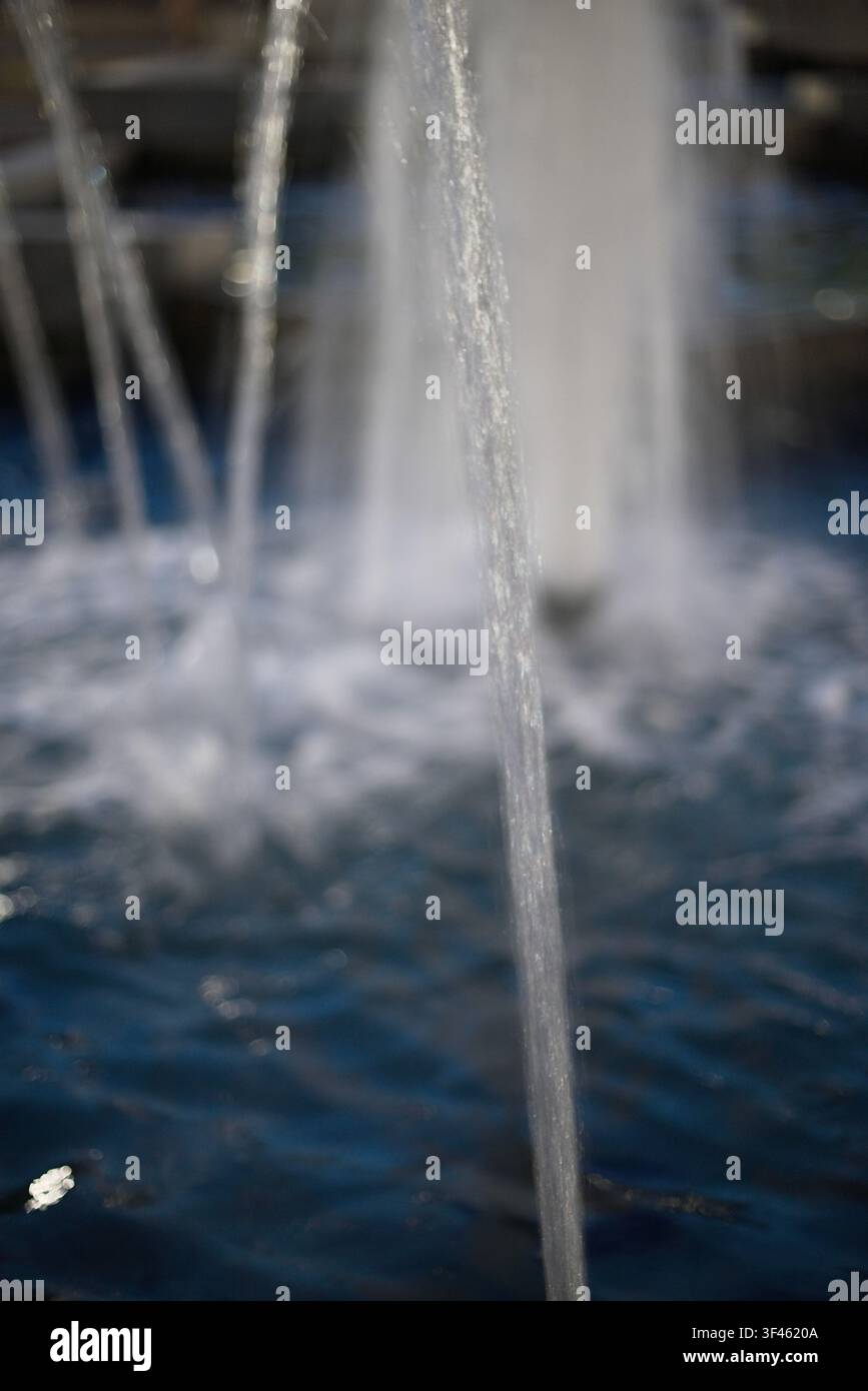 Vue rapprochée de ruisseaux d'eau claire tombant dans un bassin bleu, avec une douce mise au point floue et des éclaboussures créant un fond calme et frais. Banque D'Images