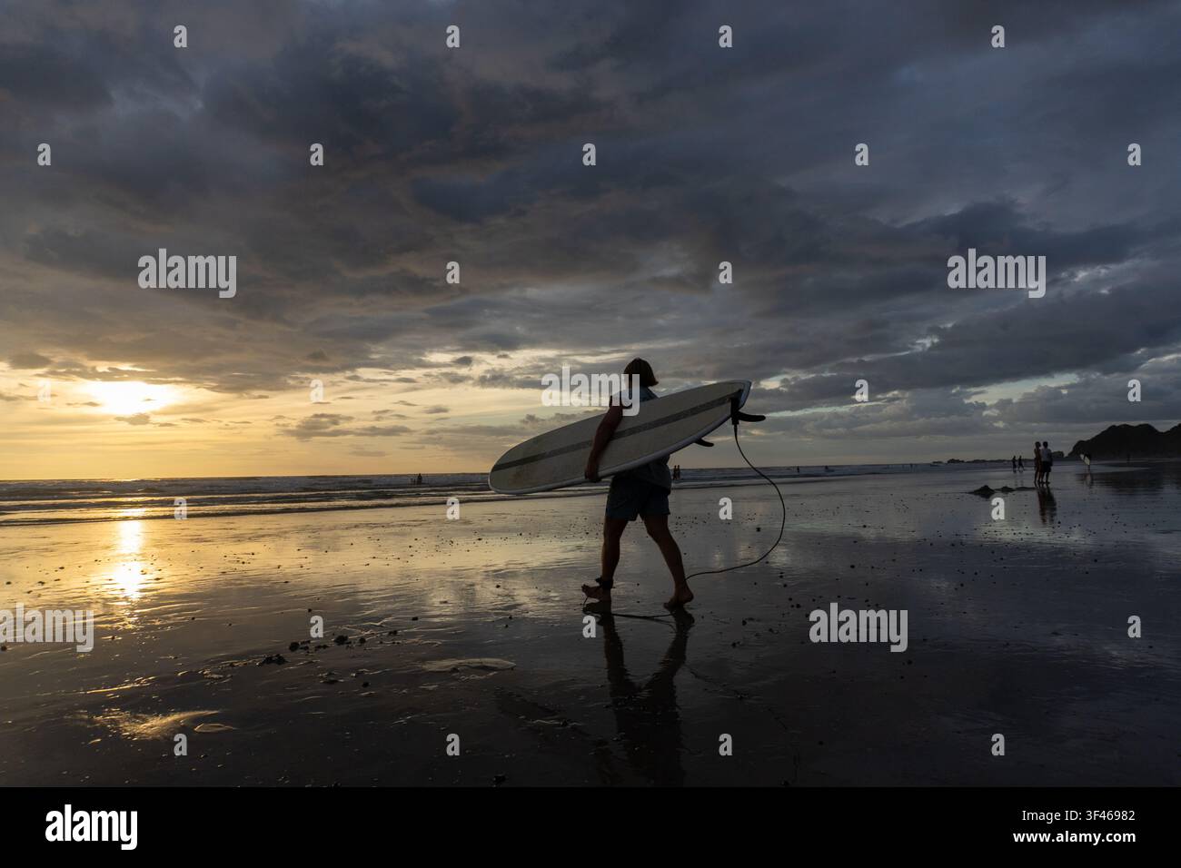 Silhouette de surfeur marchant sur la plage au coucher du soleil Banque D'Images