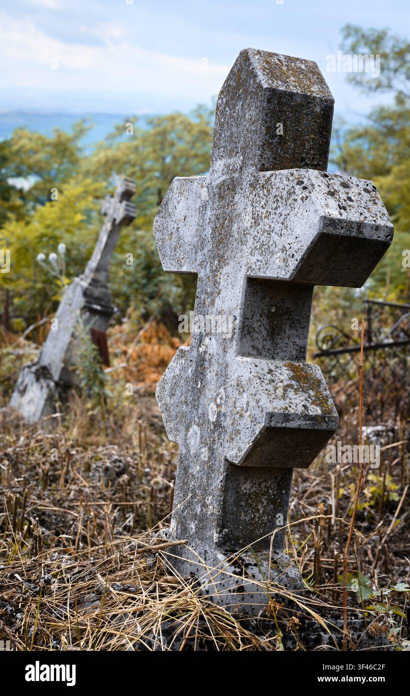 Une photographie verticale à faible angle d'un vieux croissant de pierre érodé penché dans un cimetière envahi par la végétation. Le monument fortement texturé est couvert de lichens Banque D'Images
