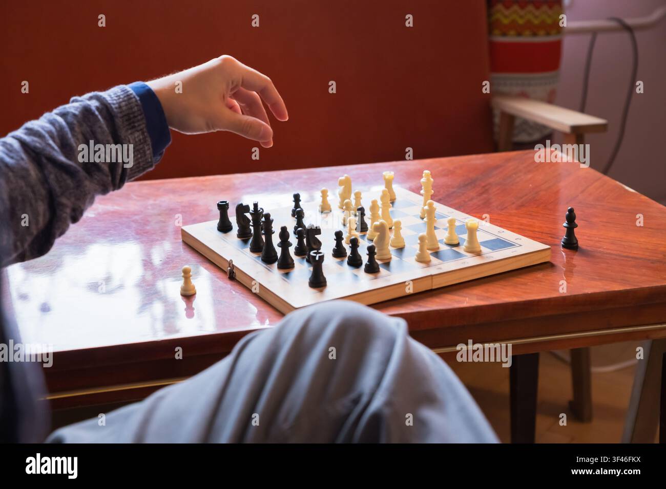 Homme jouant aux échecs sur une table en bois. Joueur déplaçant une pièce sur l'échiquier. Pensée logique et jeu de stratégie. Activité de loisir intérieure et intellectuelle Banque D'Images