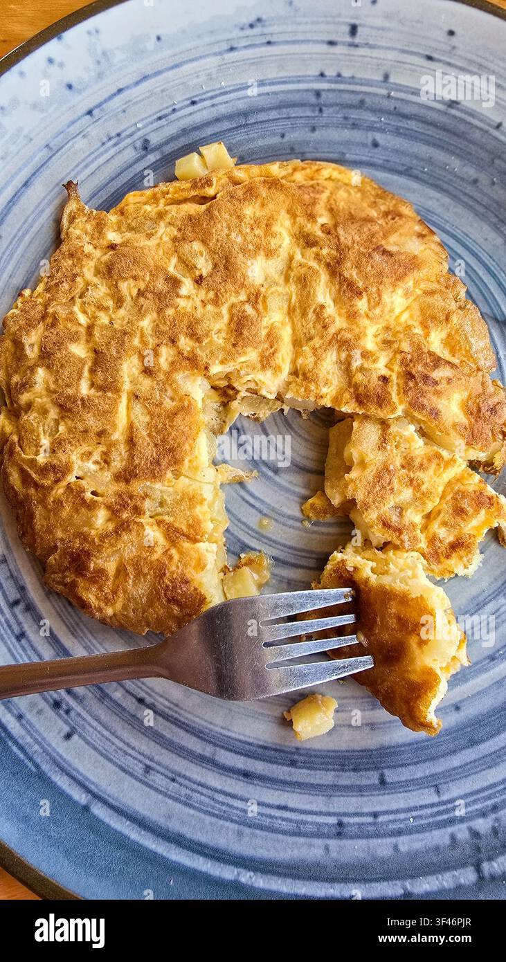 Tortilla espagnole fraîche sur une assiette bleue élégante avec fourchette Banque D'Images