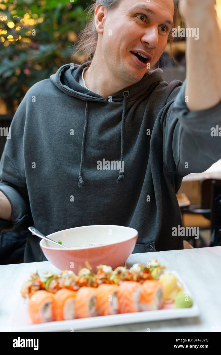 Homme assis à une table de restaurant profitant d'une soupe chaude pendant un déjeuner décontracté. Homme concentré dînant dans un restaurant asiatique avec une expression concentrée. Atmosphère traditionnelle avec une cuisine authentique et chaleureuse Banque D'Images