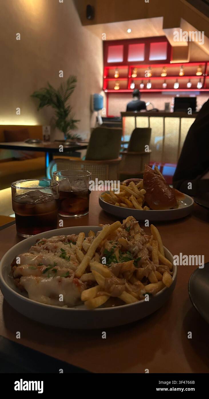 Gros plan de plats de pâtes et de boissons gazeuses servis sur une table dans un restaurant moderne avec un éclairage d'ambiance chaud et un arrière-plan intérieur flou. - Image de stock capturée avec un smartphone