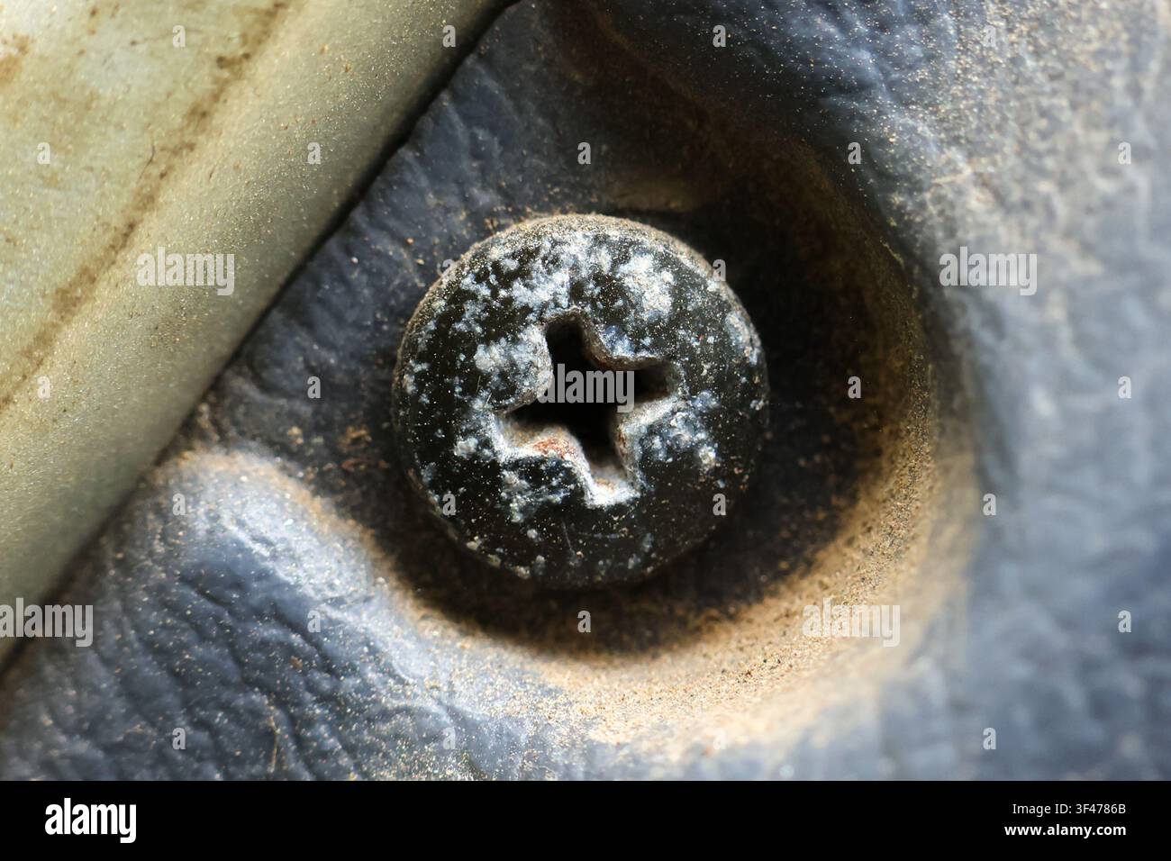 Une vis à tête cruciforme rouillée sur une surface métallique poussiéreuse en gros plan montrant la corrosion et la texture avec des tons sourds et une patine usée Banque D'Images