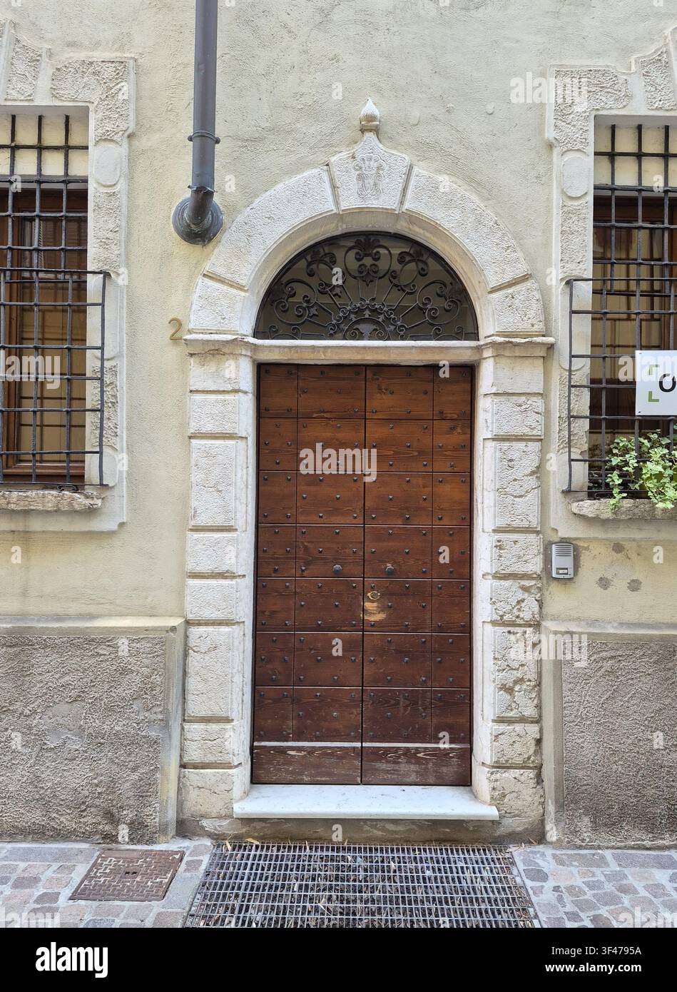 Ancienne porte en bois cloutée avec arc en pierre orné et lunette en fer située dans la vieille ville de Mantoue, Lombardie, Italie Banque D'Images