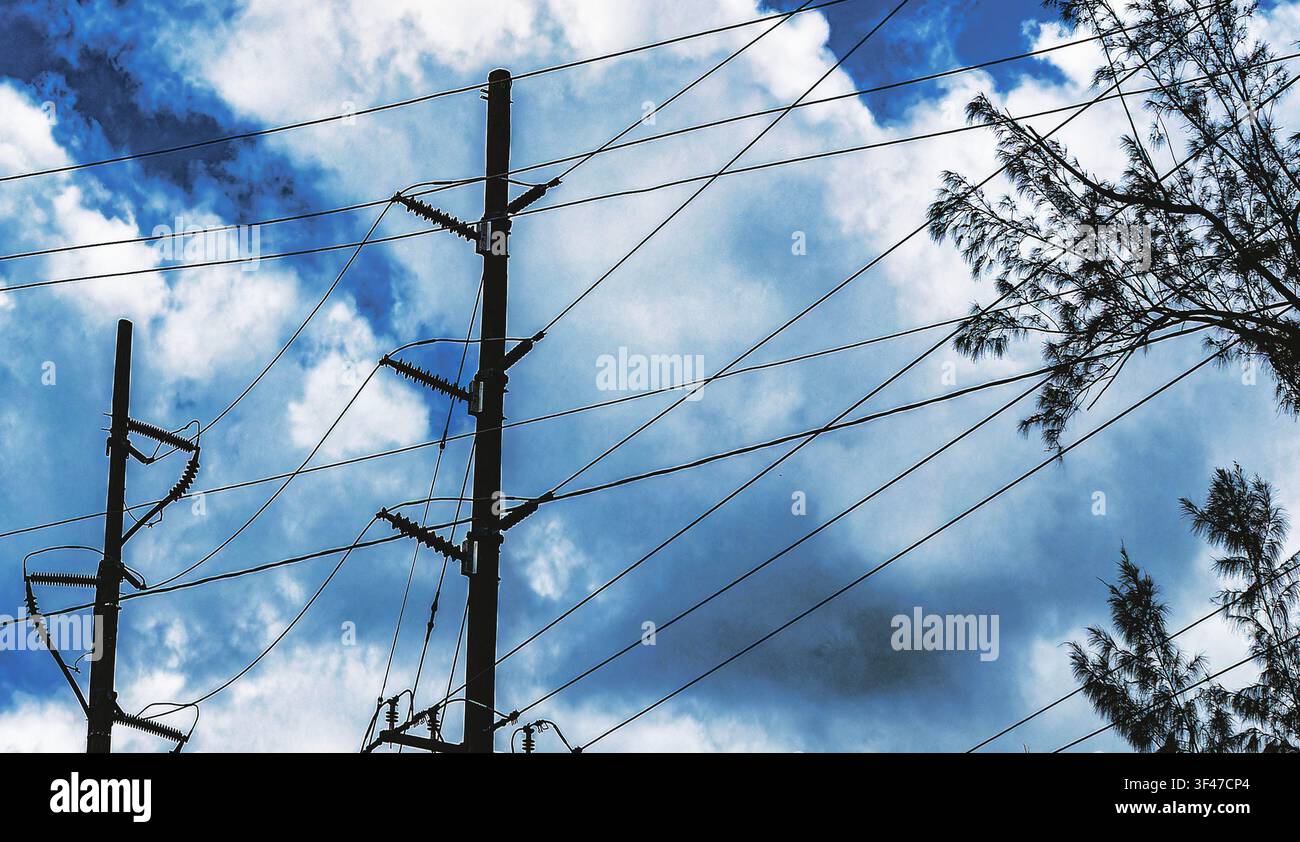 Lignes électriques et poteaux en bois sur fond de ciel bleu et nuageux. Banque D'Images
