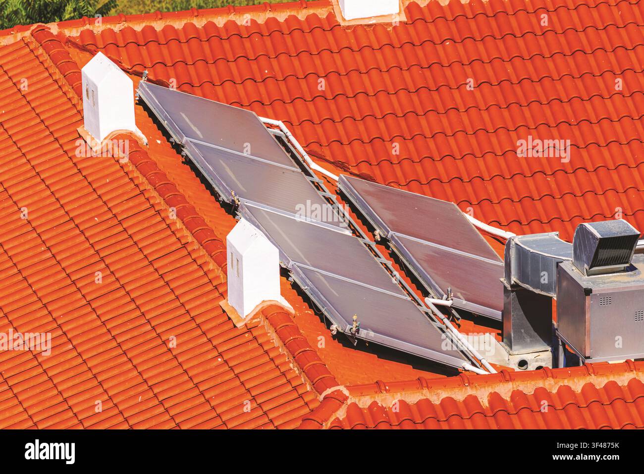 Vue rapprochée de capteurs solaires thermiques installés sur un toit en tuiles rouges avec cheminées. Crète. Grèce. Banque D'Images