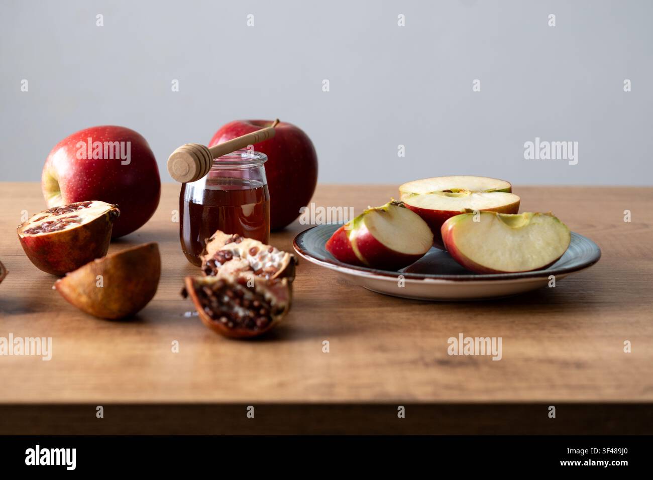 Nature morte pour Rosh Hashanah avec des tranches de pomme rouges, un pot de miel avec un loucheur et un grenade sur une table en bois, symbolisant une douce célébration juive du Nouvel An Banque D'Images