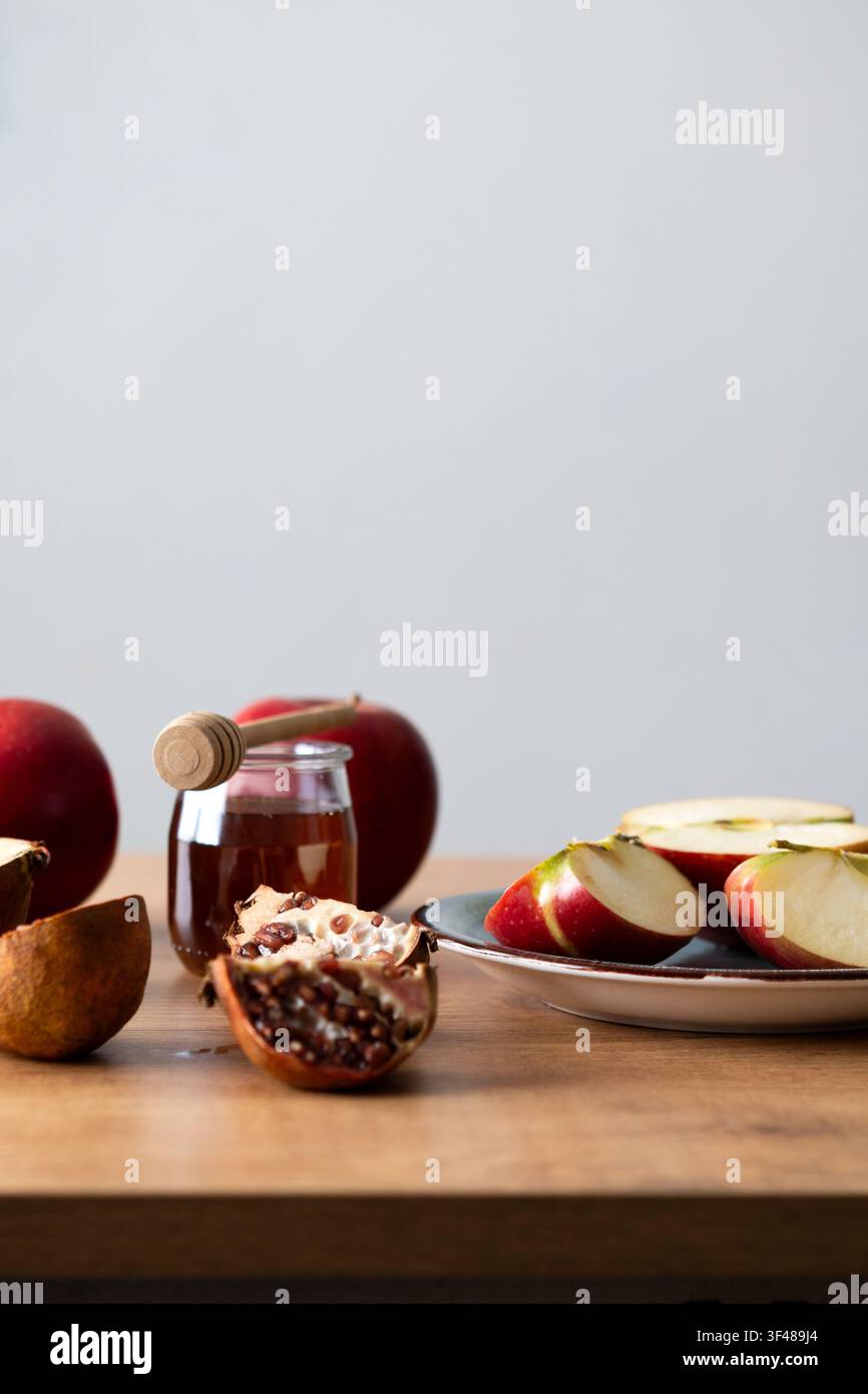 Nature morte minimaliste pour Rosh Hashanah avec des tranches de pomme, un pot de miel et une cuillère, et un grenade sur une table en bois, symbolisant une douce Nouvelle Année juive ce Banque D'Images