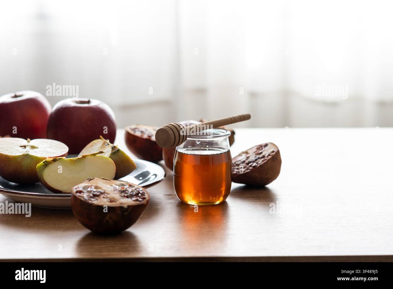 Nature morte traditionnelle pour Rosh Hashanah avec des tranches de pomme, un pot de miel et un cuillère, et un pamplemousse sur une table, symbolisant une douce célébration du Nouvel An juif Banque D'Images