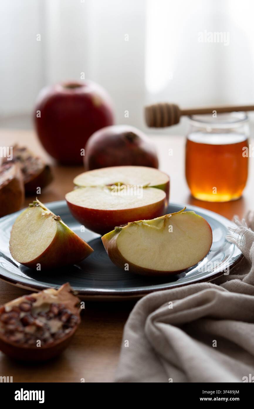 Nature morte en gros plan d'une pomme tranchée sur une assiette avec un pot de miel et une cuillère sur une table en bois, symbolisant un Rosh Hashanah sucré, la Nouvelle Année juive celebra Banque D'Images