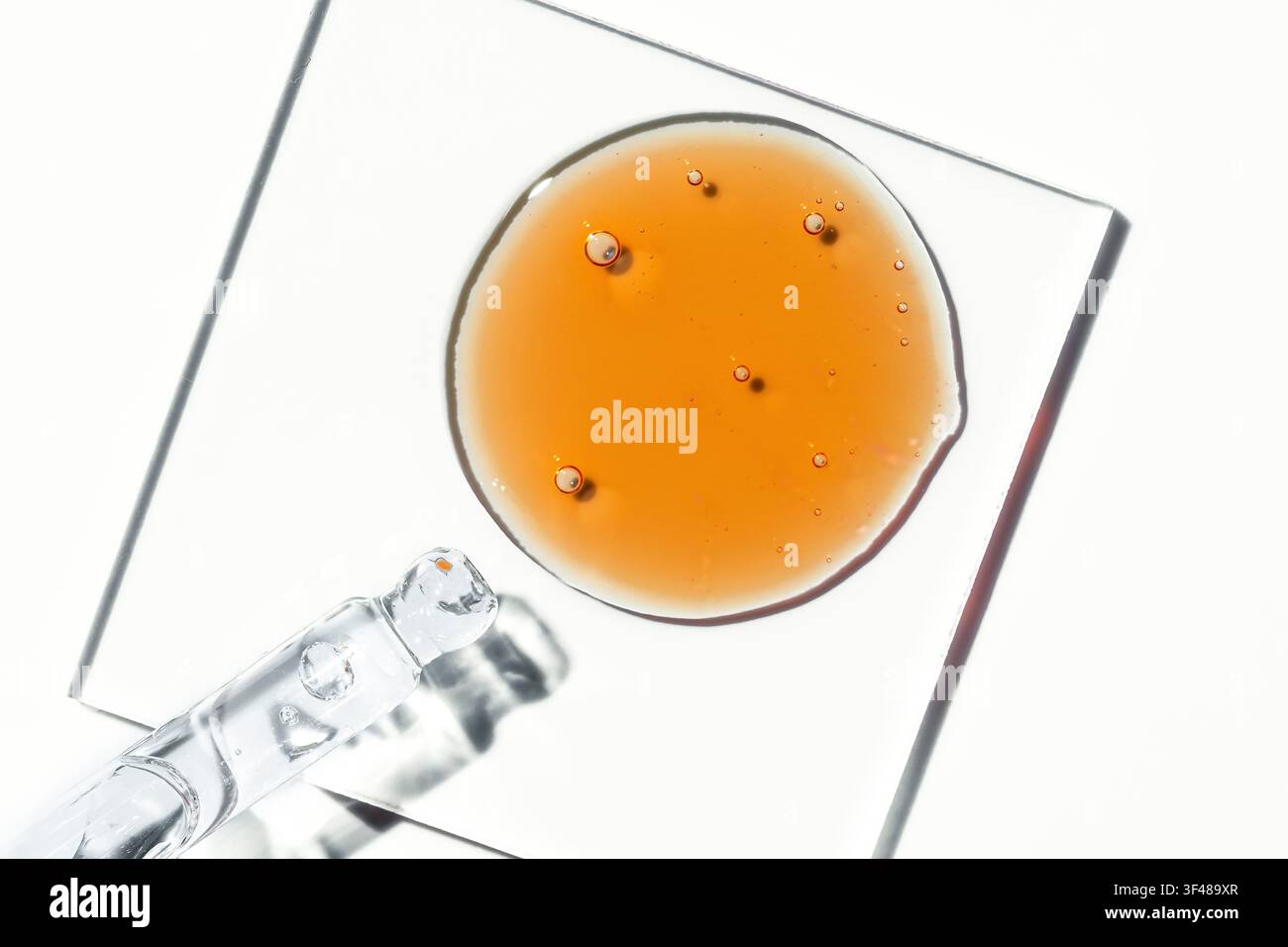 Macro gros plan de sérum visage au vitamine C avec gouttes d'huile et bulles cosmétiques sur une plaque de verre, concept de soins minimaux sur fond blanc éclatant, cl Banque D'Images