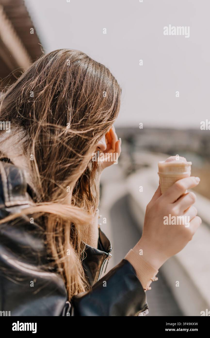 Femme vendant de la glace, jeune femme aux cheveux fluides tenant une boule de glace rafraîchissante tout en profitant d'une journée ensoleillée en plein air Banque D'Images
