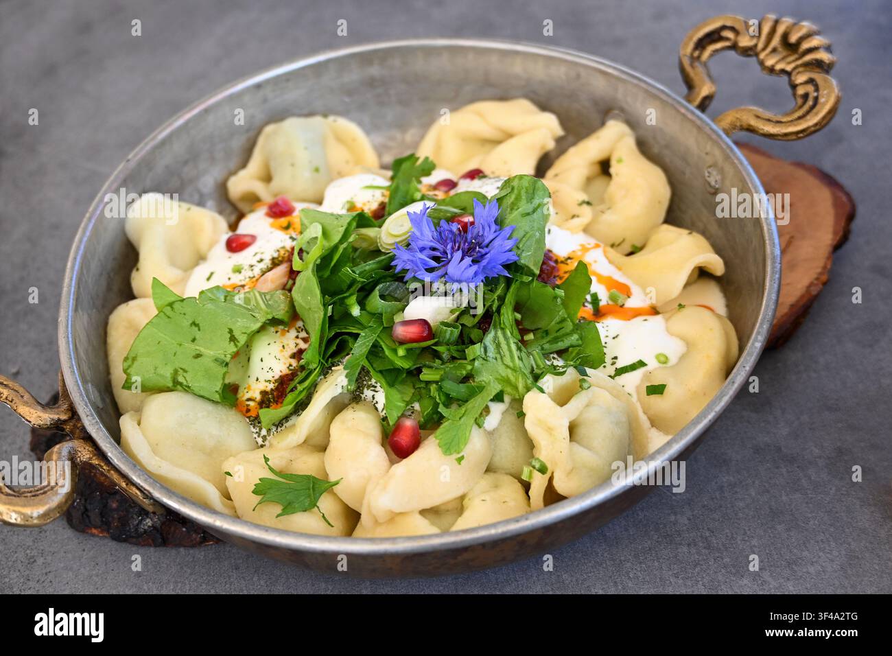 Manti, plat turc composé de boulettes farcies, servi avec une sauce au yaourt à l'ail et une salade de laitue, garni d'une fleur bleue de bleuet Banque D'Images