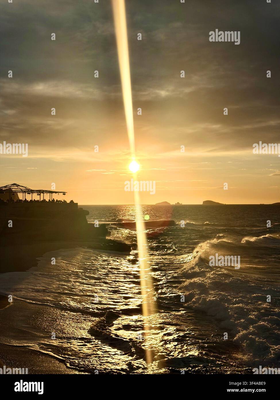 Éclat de soleil dramatique sur les vagues se brisant dans un club de plage au sommet des falaises, Ibiza, Espagne Banque D'Images