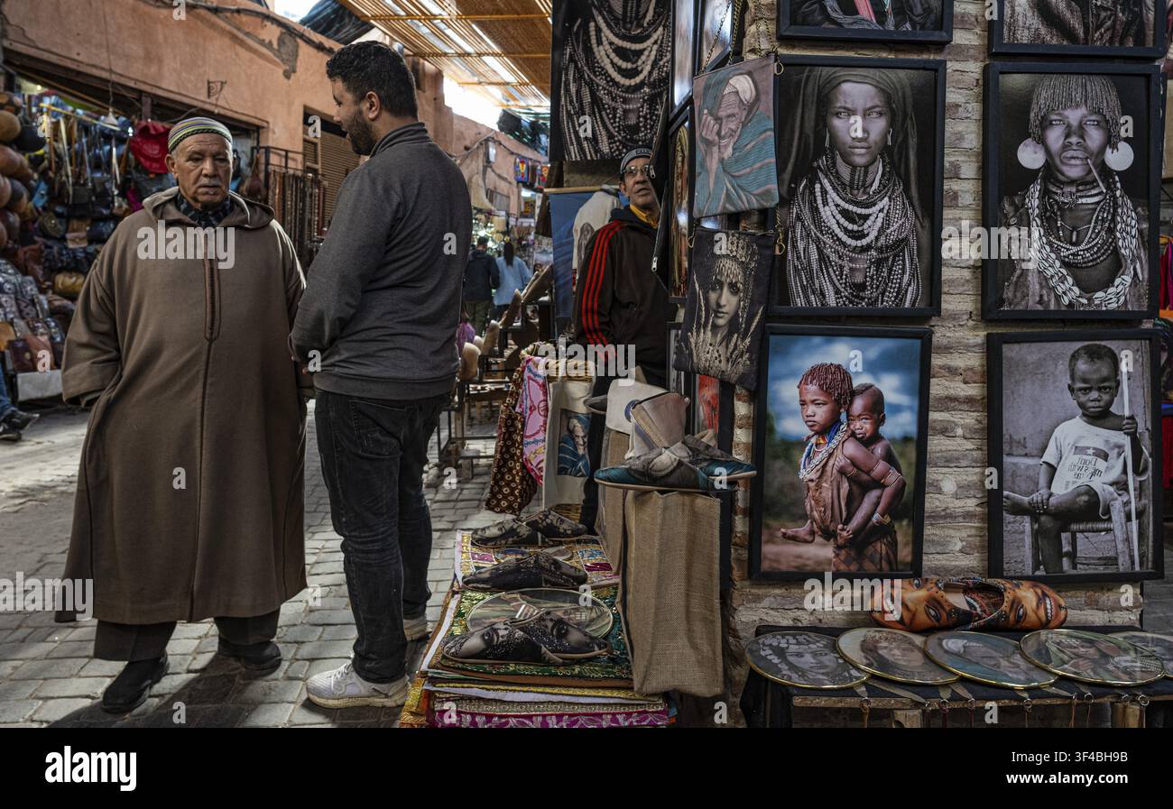 Deux hommes marocains discutent dans le souk, bazar à côté d'une boutique vendant des tableaux, des dessins de personnes en Afrique, souk, bazar, Marrakech, Maghreb, Maroc, Non Banque D'Images