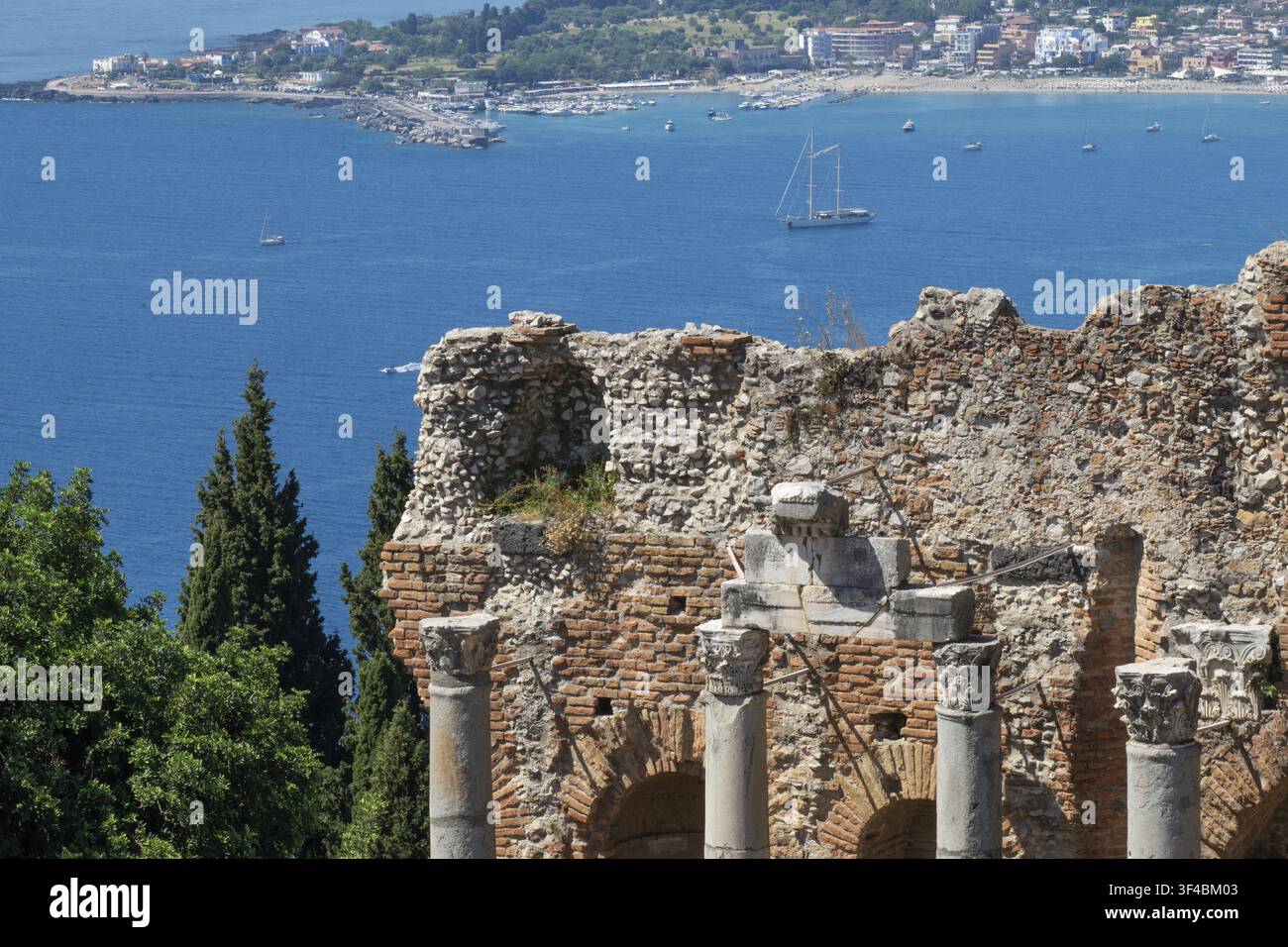 Vue des piliers du théâtre antique de Naxos et du voilier Chronos à l'ancre, Taormine, Sicile, Italie Banque D'Images
