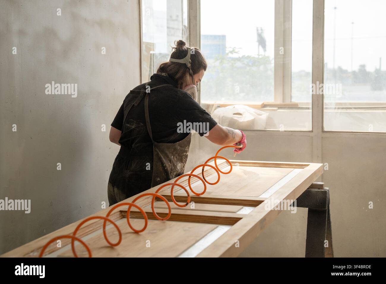 Charpentier professionnel souffle la poussière d'une porte en bois antique restaurée avec un tuyau à air dans l'atelier de peinture Banque D'Images