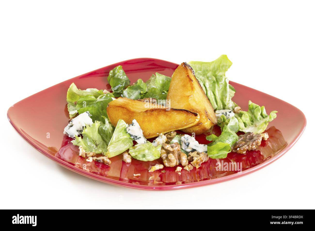 Salade avec poires caramélisées, noix et fromage bleu, sur une assiette rouge, isolée sur fond blanc Banque D'Images