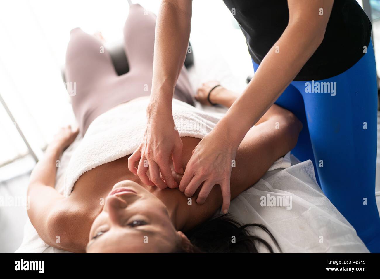Femme adulte recevant un massage ciblé du cou et des épaules dans un studio de bien-être lumineux, le thérapeute exerce une pression douce sur le trapèze et la base du crâne Banque D'Images