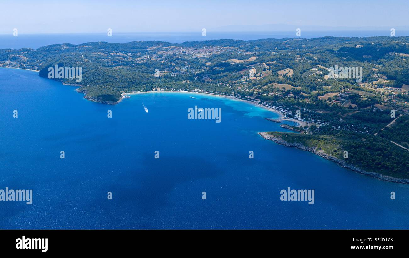 Une vue aérienne élevée montre une baie bleue incurvée, une plage pâle et des collines boisées parsemées de maisons côtières à Golden Beach sur Kassandra à Halkidiki, en Grèce. Banque D'Images
