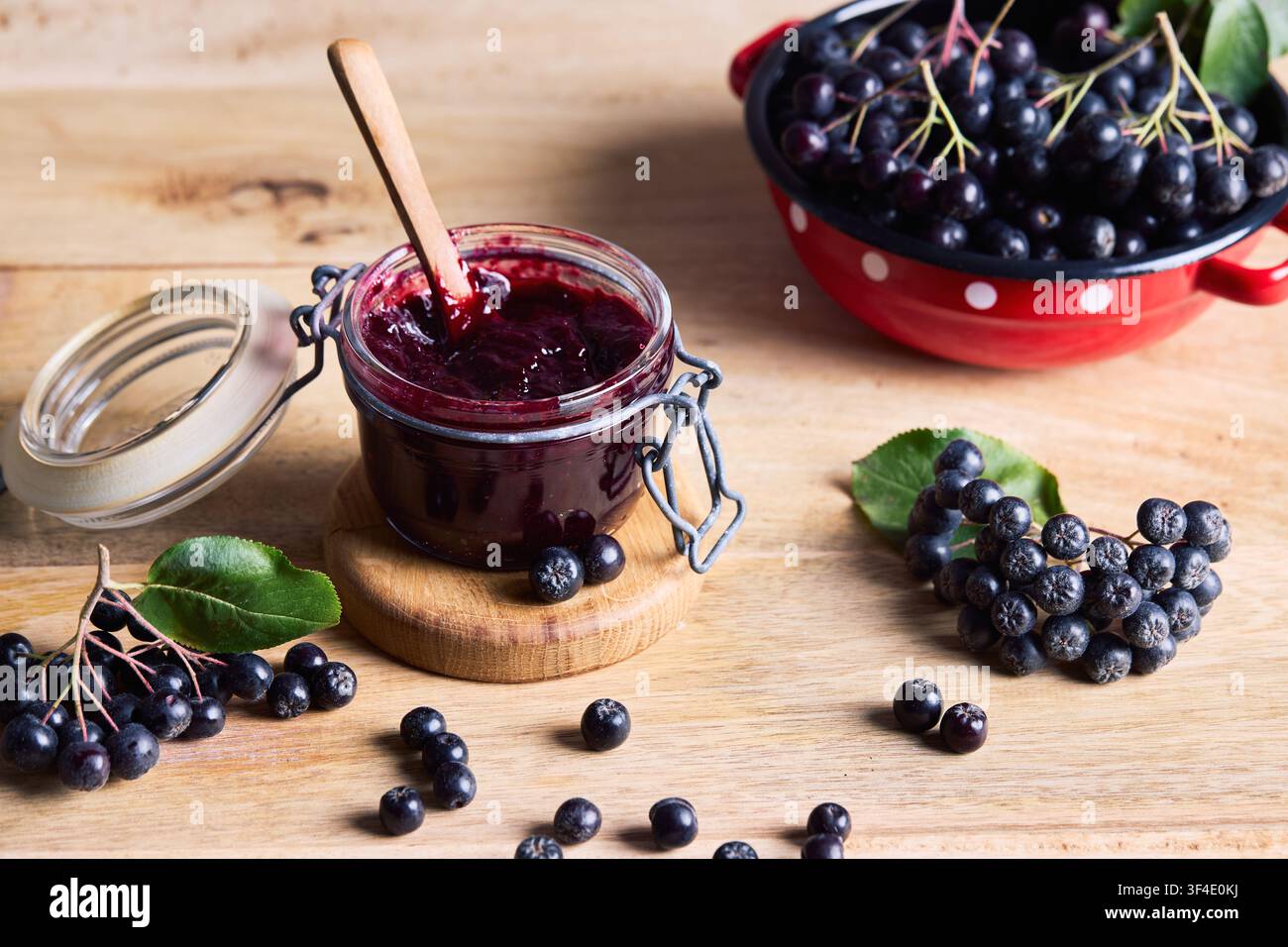Confiture maison de baies d'aronia dans un pot en verre ouvert avec des baies d'aronia noires fraîches sur une table en bois. Aliments biologiques maison, récolte saisonnière et superaliments Banque D'Images
