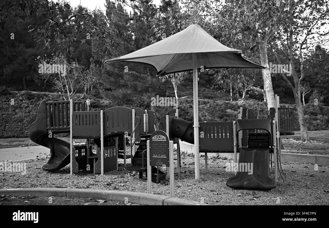 Aire de jeux noir et blanc sous un grand auvent. Glissades et structures d'escalade pour enfants visibles. Des arbres encadrent l'arrière-plan. Les parterres de jardin entourent t Banque D'Images