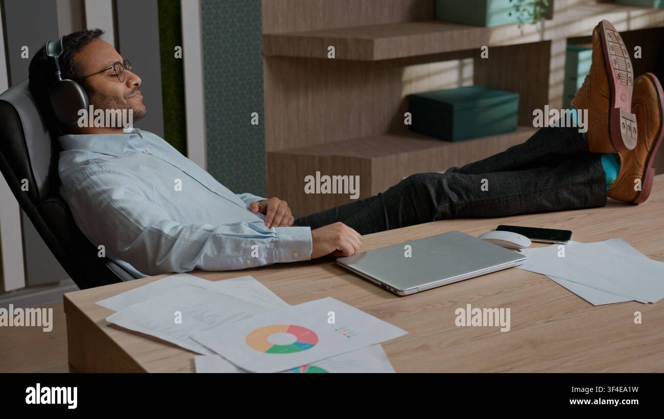 Homme d'affaires indien arabe détendu écoutant de la musique avec des écouteurs sans fil au bureau, homme d'affaires profitant d'une pause après le travail, calme Banque D'Images