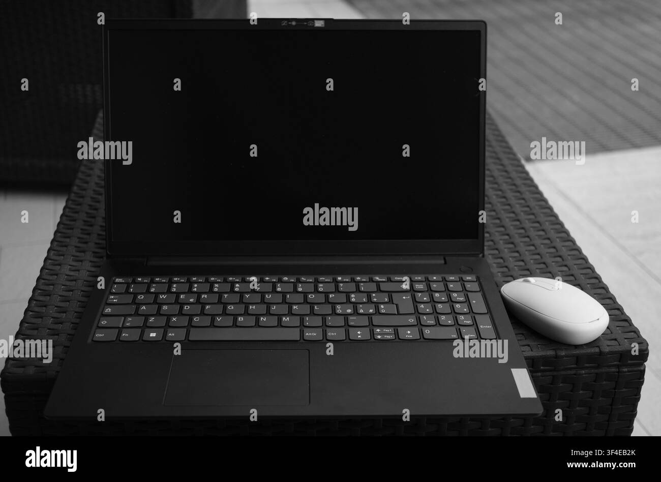 Photo en noir et blanc montrant un ordinateur portable ouvert avec un écran sombre. Une souris d'ordinateur blanche repose à côté du clavier. L'appareil est posé sur un panier en osier tressé Banque D'Images