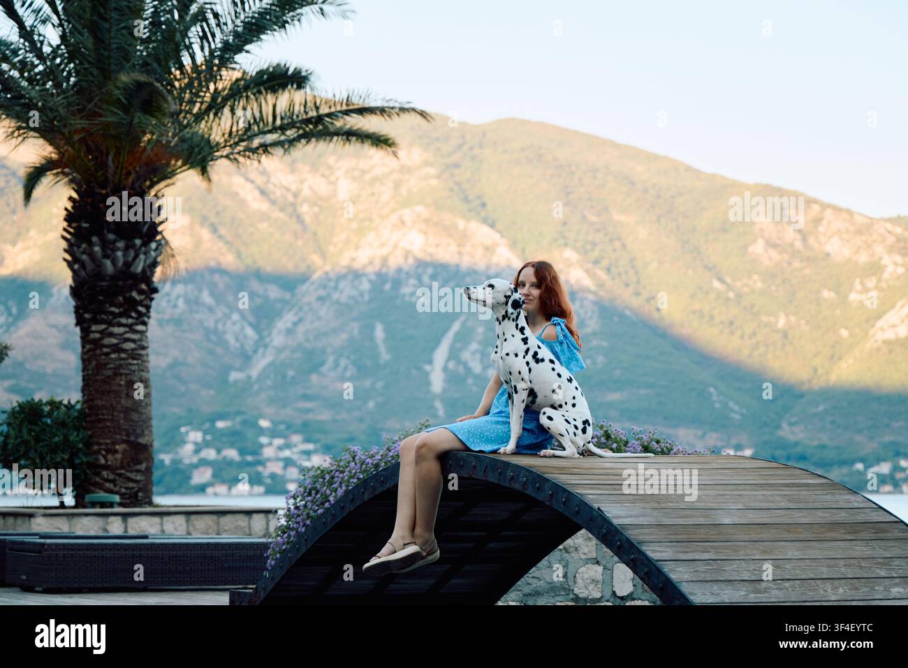 Une femme profite de moments paisibles avec son Dalmatien au-dessus de la mer Adriatique. Un paysage méditerranéen avec des montagnes et des palmiers capture une détente Banque D'Images