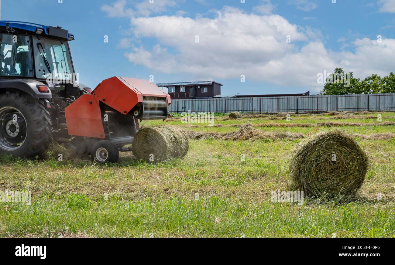 Machine à baller les foins produisant une boule ronde pendant la récolte estivale des champs Banque D'Images