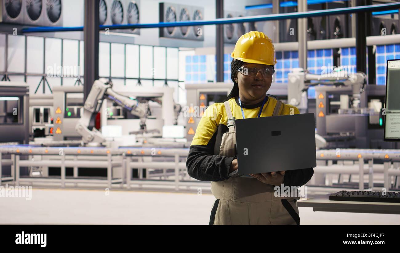 Spécialiste souriant de l'usine intelligente testant des systèmes automatisés pour garantir la fiabilité. Ingénieur heureux dans une usine industrielle 4.0 identifiant les goulots d'étranglement et optimisant les engrenages sur la base des données, caméra A Banque D'Images