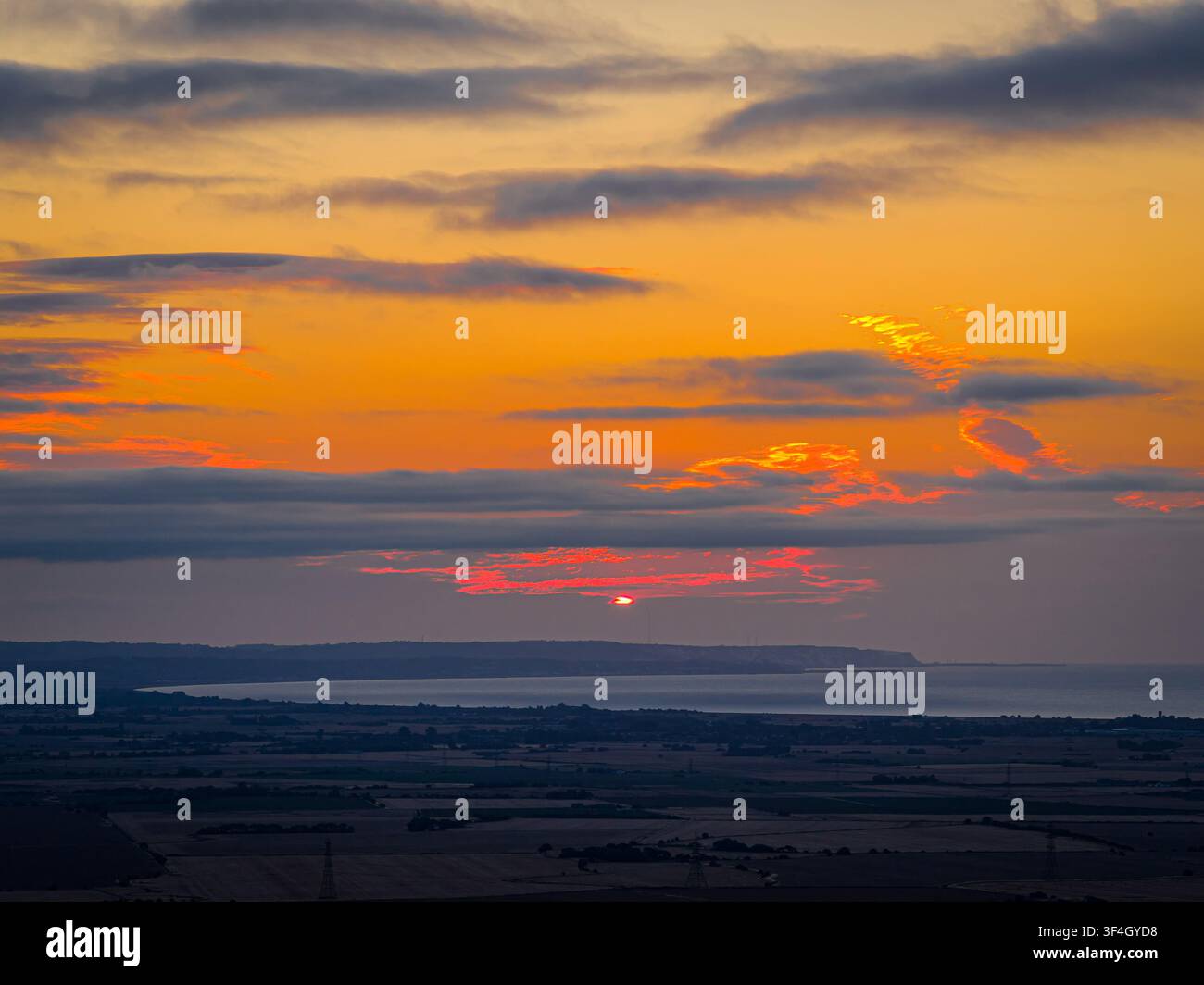 Couchant ardent brille à travers les nuages superposés au-dessus des terres agricoles rurales et d'une côte lointaine du Sussex ; idéal pour les publicités de voyage, de nature, de climat et de campagne Banque D'Images