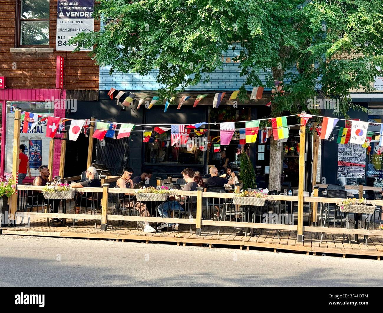 Les clients sont assis sur une terrasse de restaurant extérieure décorée de drapeaux internationaux sur le boulevard Saint-Laurent à Montréal, au Québec, Canada Banque D'Images