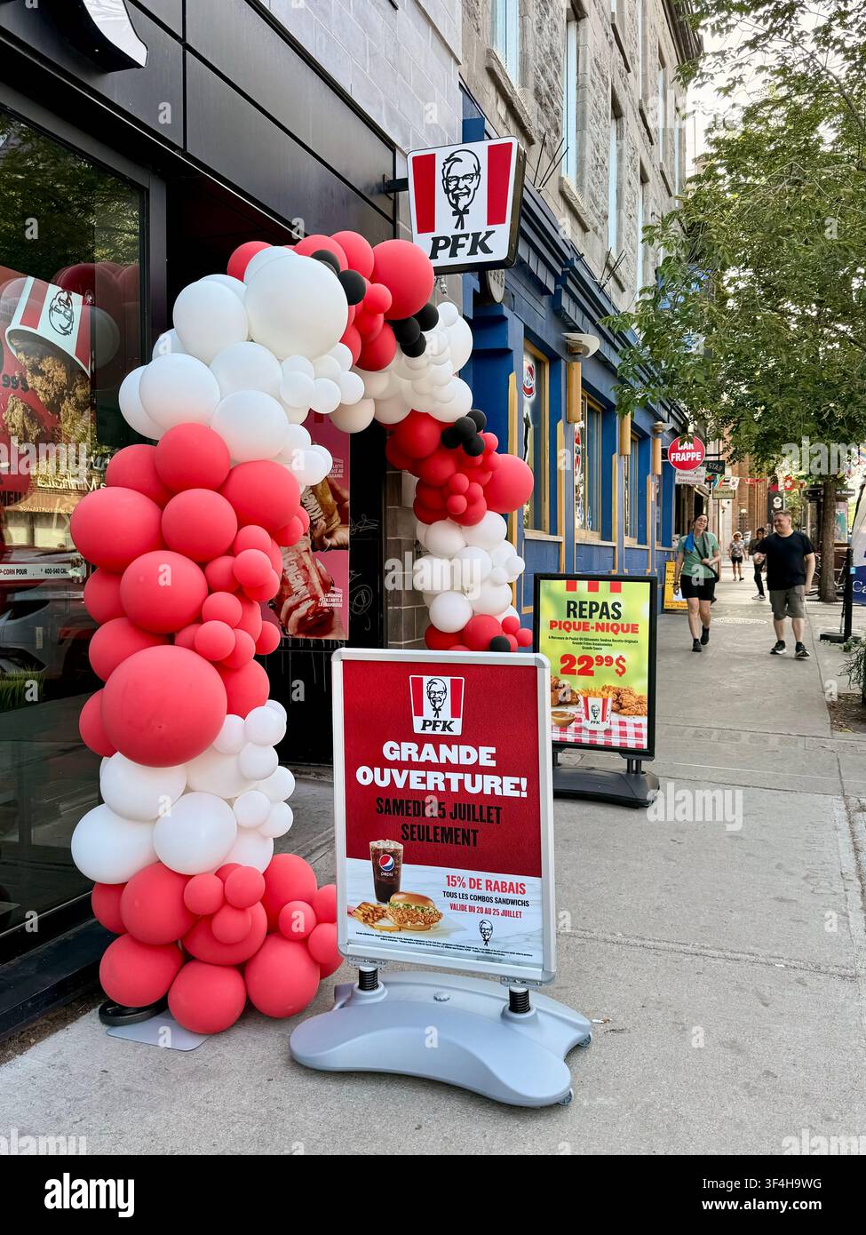 Vitrine d'un restaurant PFK/KFC nouvellement ouvert avec une arche de ballons rouge et blanc pour l'inauguration à Montréal, Québec, Canada, illustrant la restauration rapide mondiale - Image de stock capturée avec un smartphone