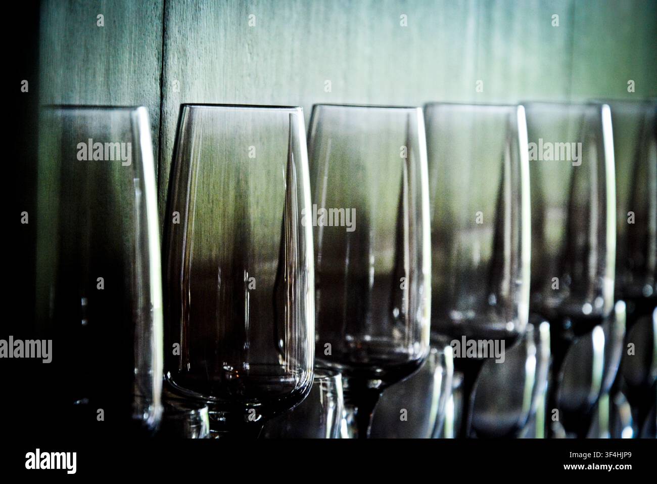 Range d’élégants verres à vin en cristal reflétant une lumière atmosphérique sur un fond texturé sombre, prise artistique avec faible profondeur de champ. Banque D'Images