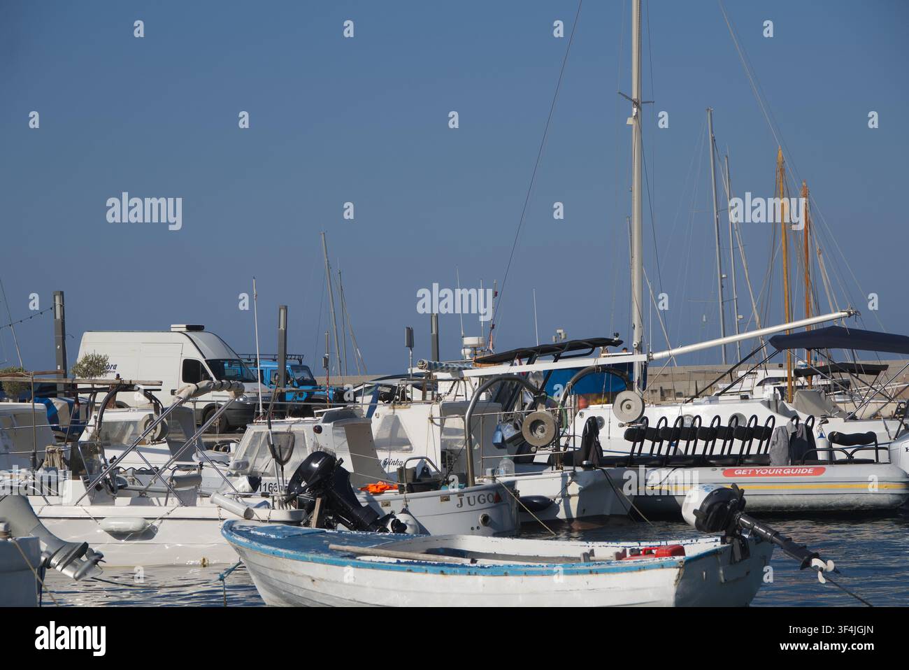 Petit bateau à rames en bois amarré dans une marina méditerranéenne animée, entouré de divers bateaux à moteur, hors-bords et yachts à voile par une journée ensoleillée et claire. Banque D'Images