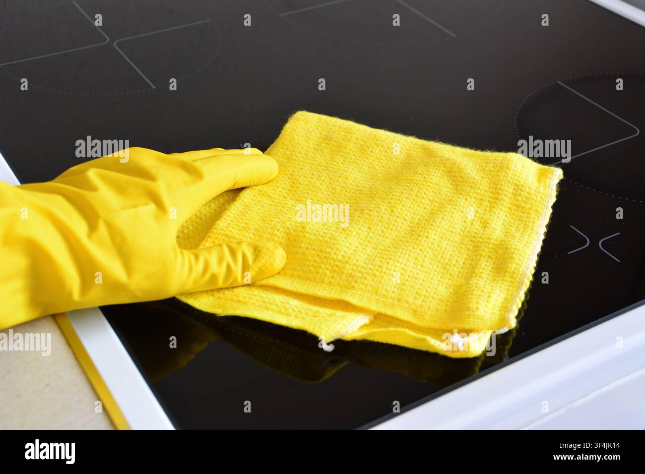 Personne en gant jaune nettoyant une plaque à induction avec un chiffon jaune Banque D'Images