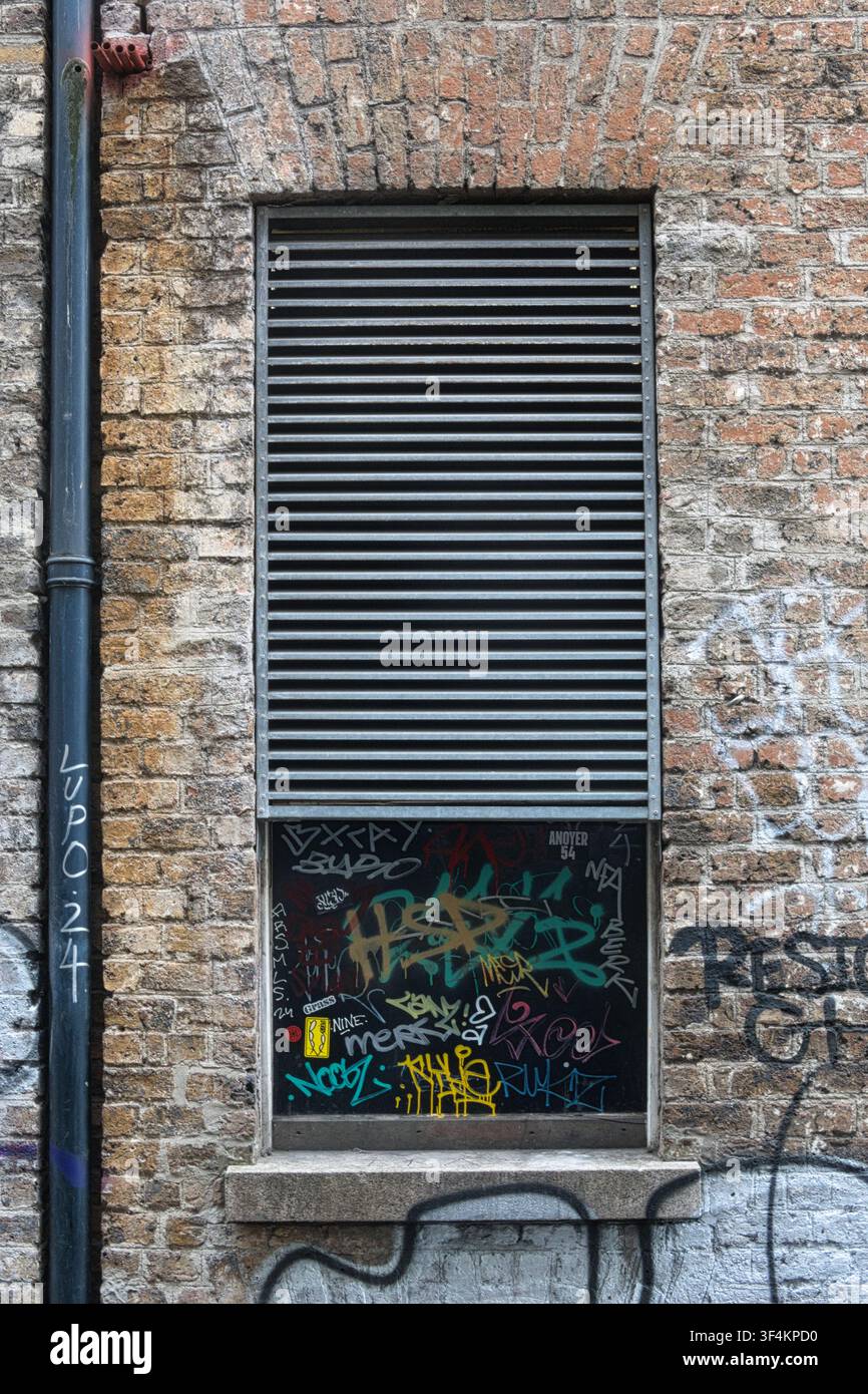 Gros plan d'un mur de briques et d'une fenêtre recouverte de persiennes métalliques et de graffitis urbains au centre de Dublin, Irlande. Banque D'Images