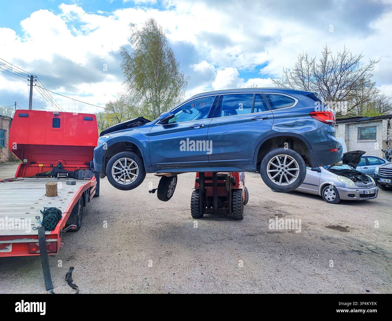 Opérations de démolition automobile : chariot élévateur déchargeant une voiture de tourisme endommagée et non roulante d'une remorque plateau Banque D'Images