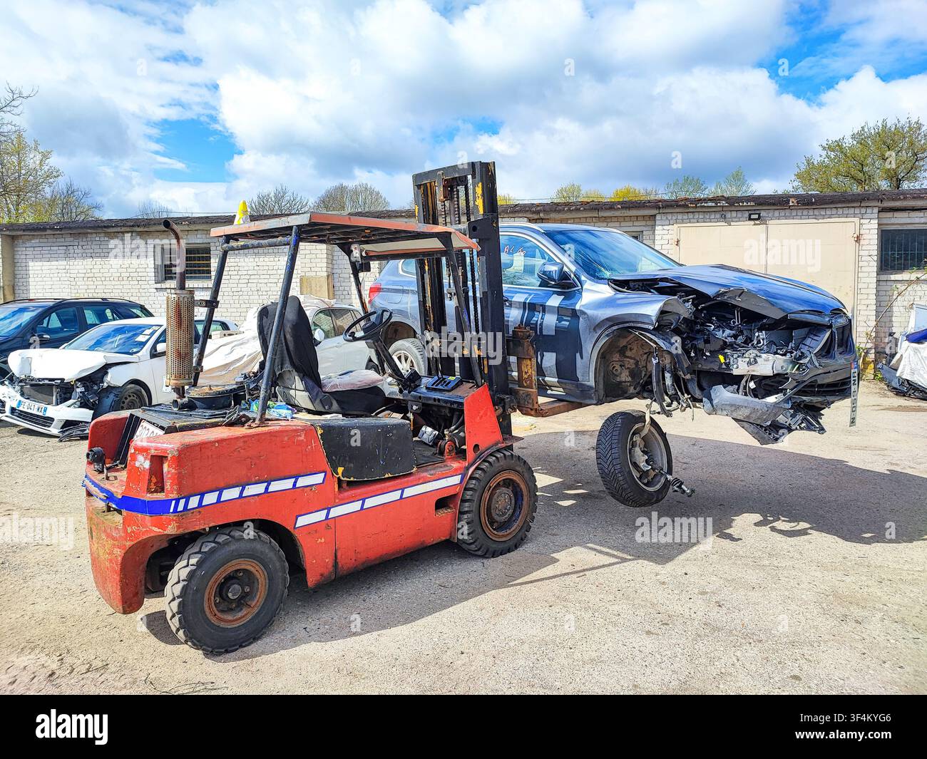 Opérations de démolition automobile : chariot élévateur déchargeant une voiture de tourisme endommagée et non roulante d'une remorque plateau Banque D'Images