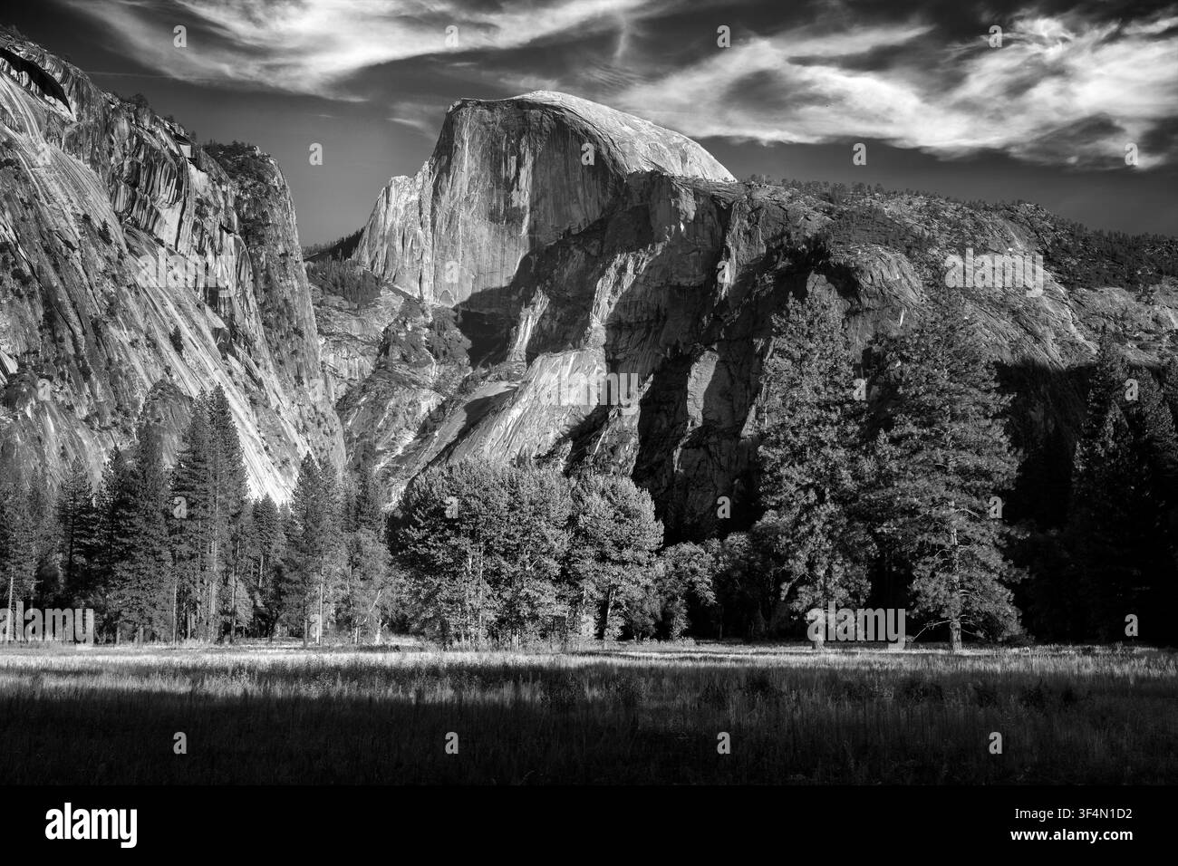 Le Half Dome se dresse majestueusement devant un fond de nuages vaporeux, sa façade de granit illuminée par le soleil de fin d'après-midi. Depuis le paisible Ahwahnee Mea Banque D'Images
