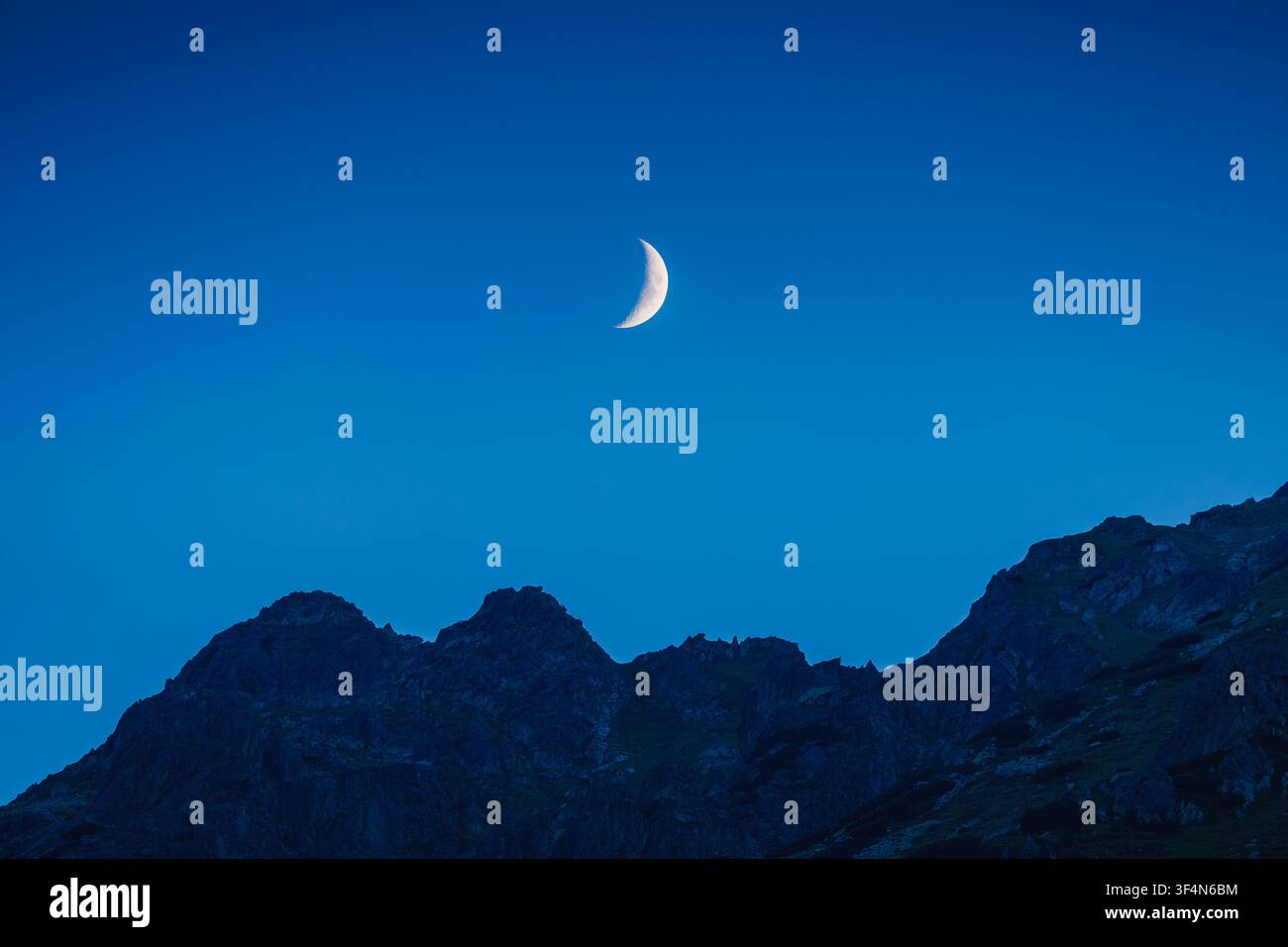 Lune croissante se levant au-dessus de la silhouette escarpée des montagnes sous un ciel crépusculaire dans les Tatras Banque D'Images