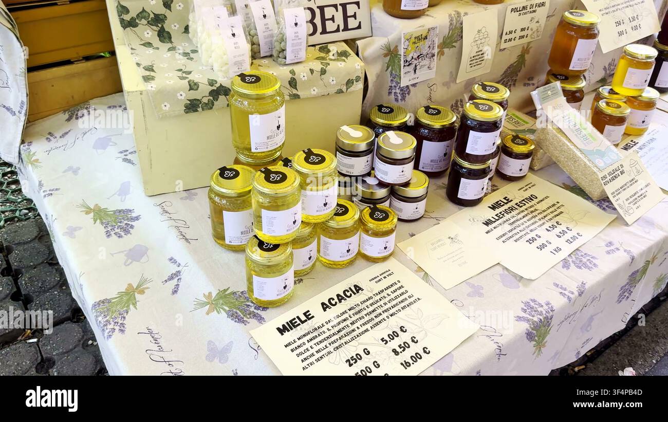 MILAN, ITALIE - 18 MAI 2024 : Plusieurs bocaux en verre de miel italien biologique et de pollen disposés sur une table de marché recouverte d'un tissu à imprimé lavande. Banque D'Images