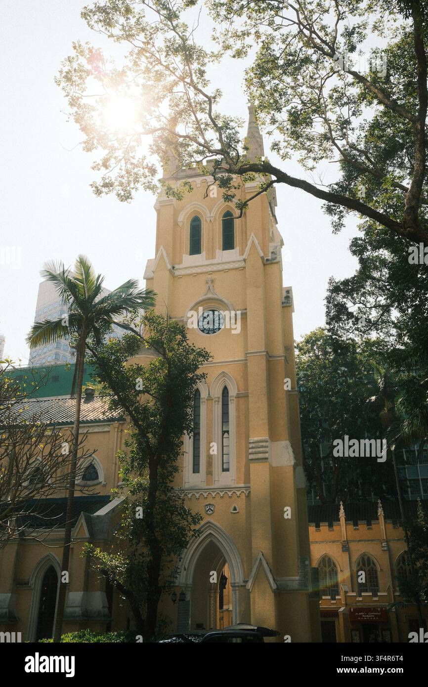 Le clocher néogothique historique peint en jaune de la cathédrale St. John's se dresse parmi des arbres verdoyants à Central, sur l'île de Hong Kong. Banque D'Images