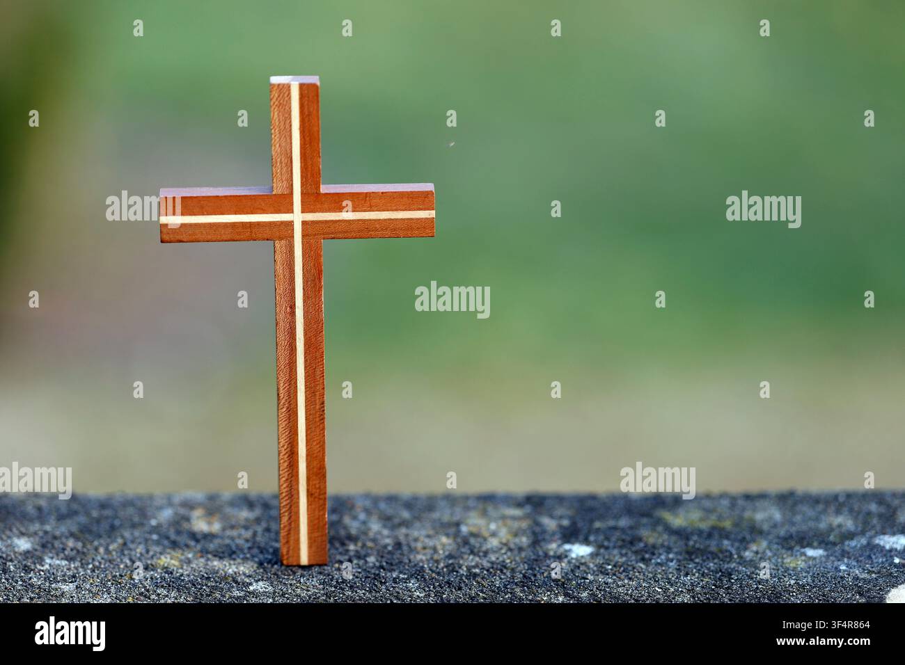 Une composition minimaliste représentant une croix en bois reposant sur une surface en granit, avec un fond flou vert. Banque D'Images