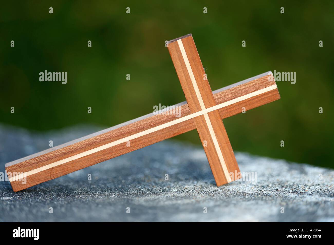 Une composition minimaliste représentant une croix en bois reposant sur une surface en granit, avec un fond flou vert. Banque D'Images