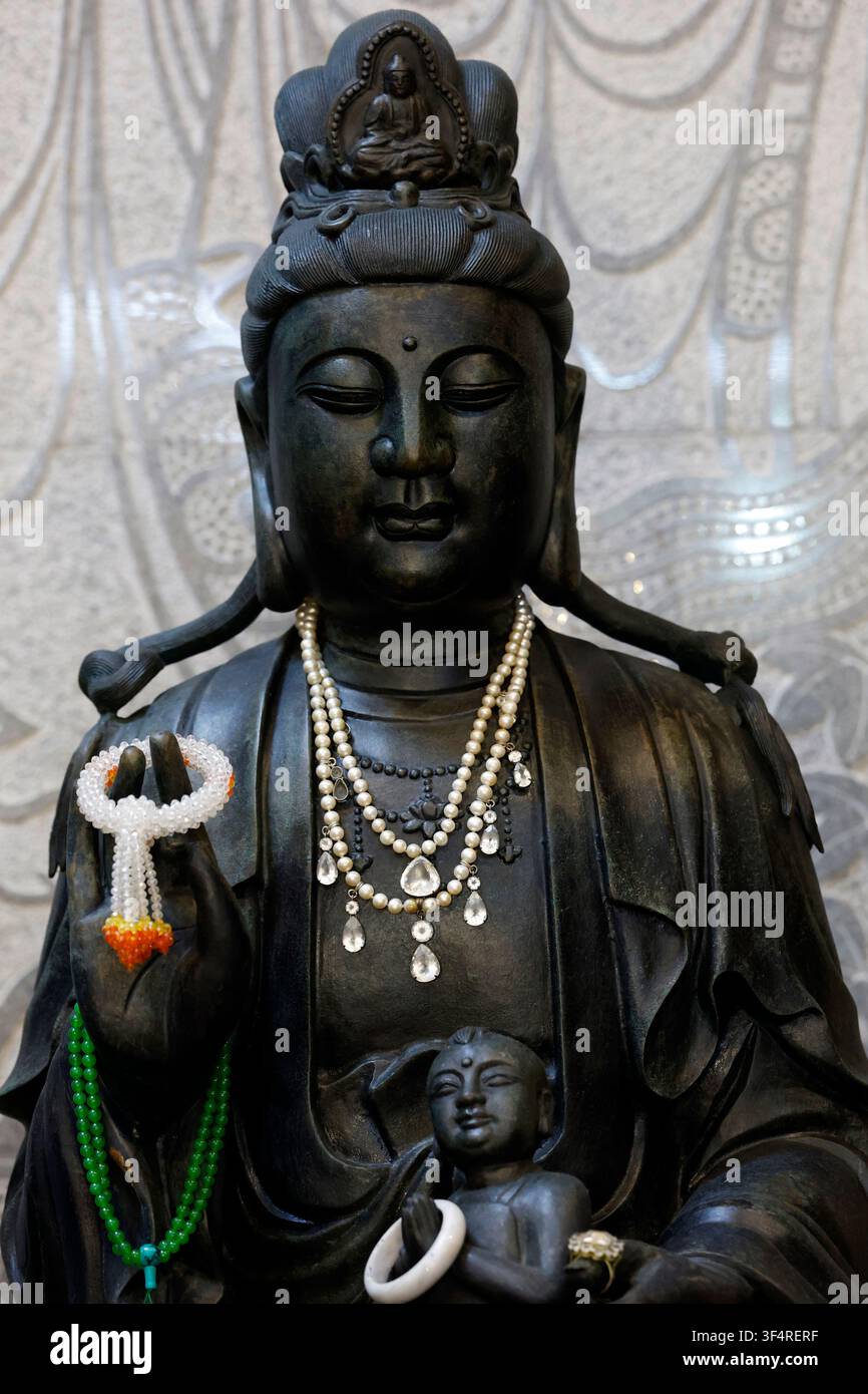 Temple chinois de Viharn Sien. Le bodhisattva Guanyin, un buste sombre orné de colliers de dévotion, protège un enfant dans ses bras – une icône de materna Banque D'Images