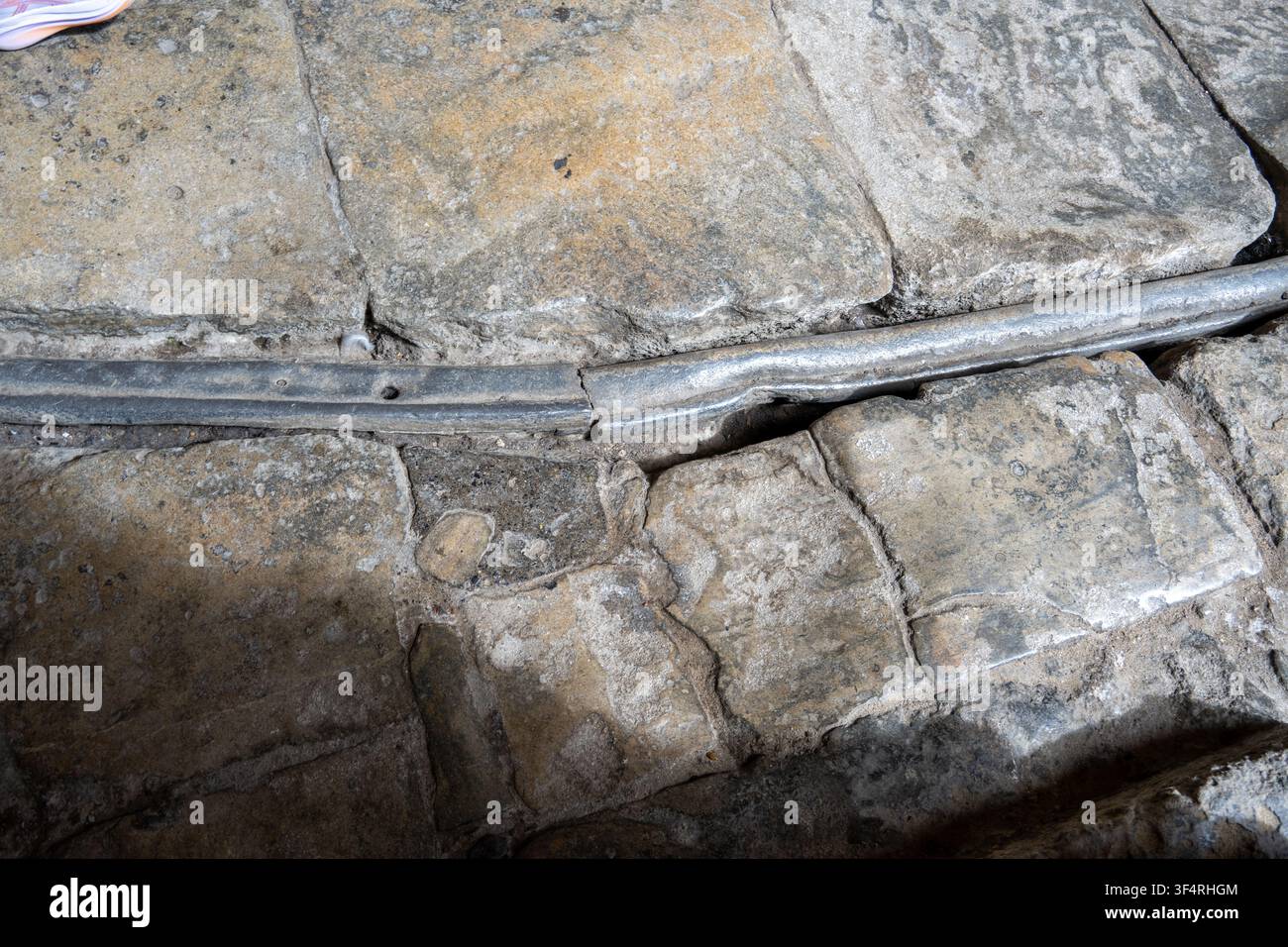 Ancien tuyau en plomb encastré dans un pavage en pierre usé sur le site archéologique des Bains Romains à Bath, en Angleterre. Banque D'Images