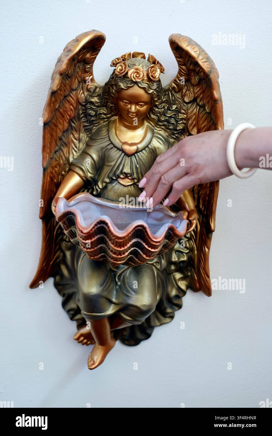 Une statue dorée d'un ange, ornée d'une couronne de fleurs, tient un bénitier. Cet objet religieux, qui contient de l'eau bénite, se trouve à Banque D'Images